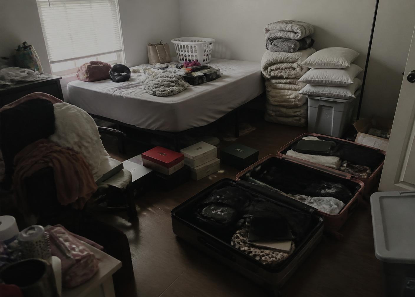 Cluttered bedroom with suitcases, blankets and shoe boxes on the floor
